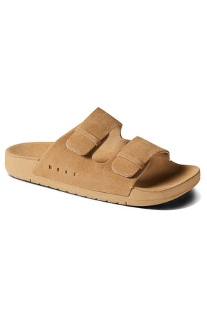 The REEF Ojai Two Bar is a tan suede sandal with two adjustable Velcro straps and a cushioned sole for support, displayed at an angle on a plain white background.
