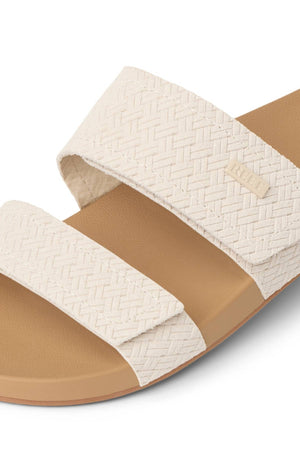 Close-up of the REEF Velcro Vista Se sandal in beige, featuring two wide textured woven straps with a small rectangular side label and a tan cushioned midsole.