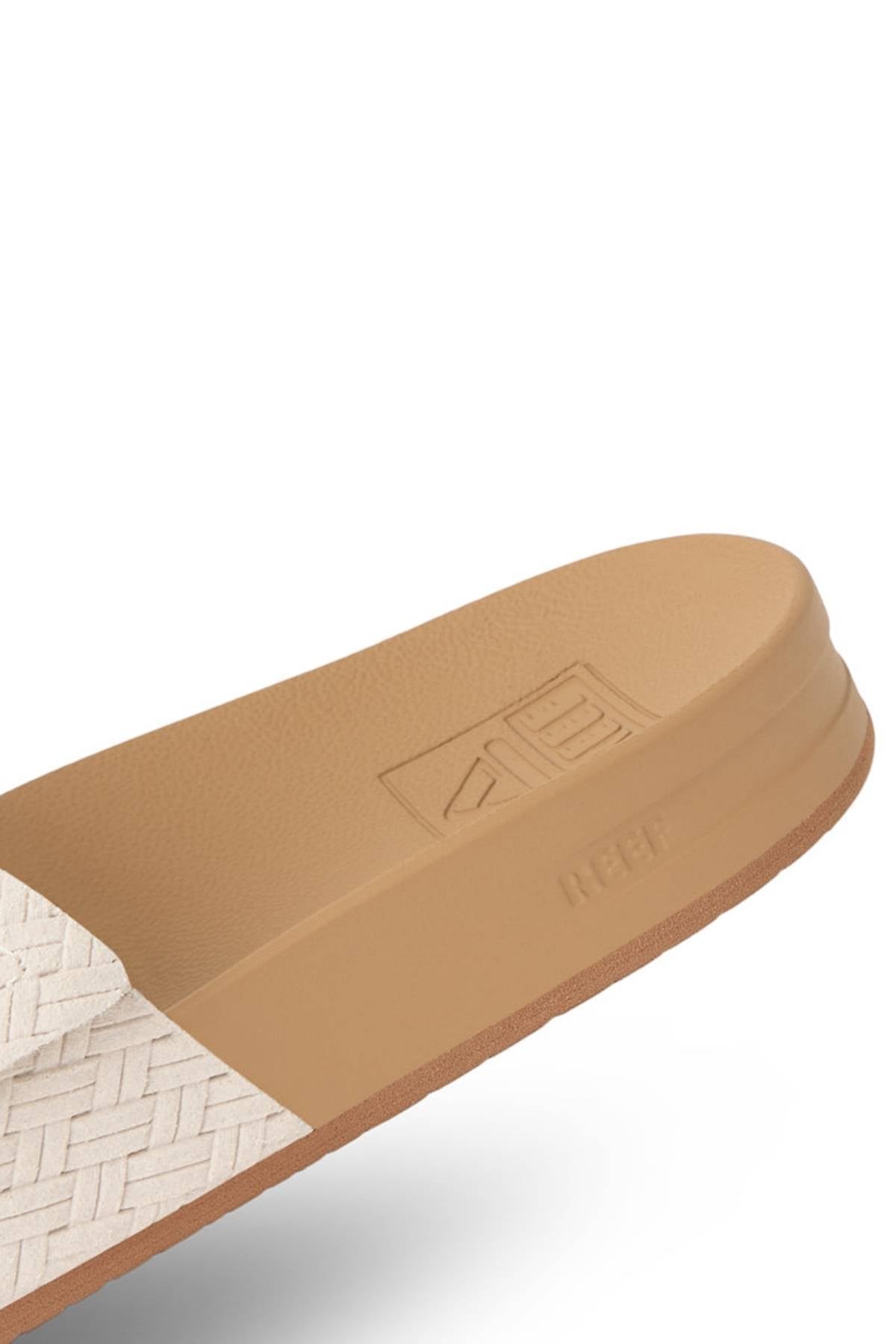 A close-up of the REEF Velcro Vista Se showcases its woven textured strap and raised sole logo, featuring a modern minimal design with an eco-friendly cushion midsole for comfort.