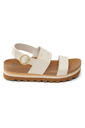 The REEF Vista Hi Buckle is a cream vegan leather sandal with wide toe and ankle straps, circular buckle, thick supportive sole, tan/brown ridged outsole for arch support, shown side view on a white background.