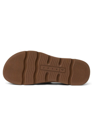 Bottom view of the REEF Vista Luxe Thea shows a brown rubber sole with textured grooves, wavy traction patterns, and a central rectangular section featuring raised letters and symbols.