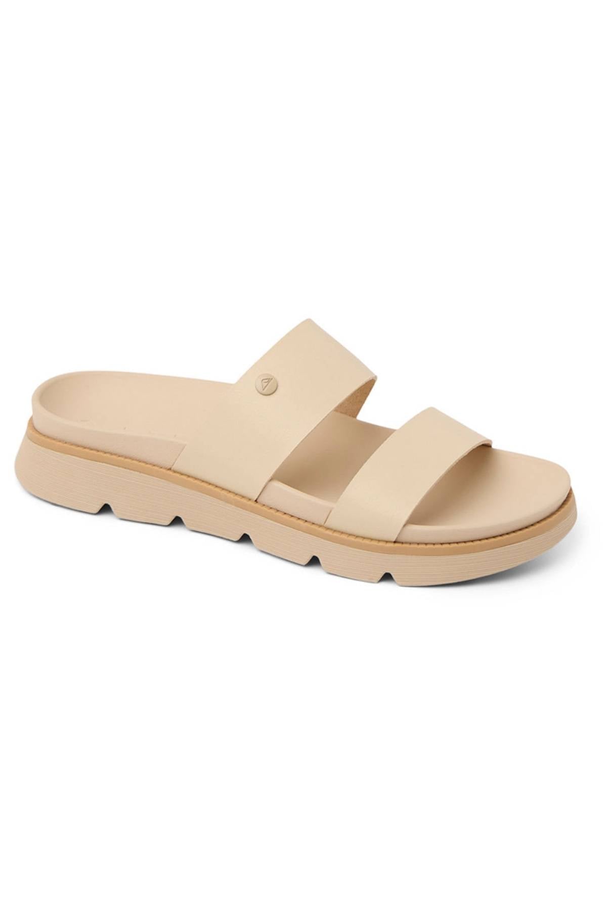 The REEF Vista Luxe Thea sandals feature two wide beige vegan leather straps, a comfy footbed, a slightly raised cushioned sole, and subtle tread details underneath.