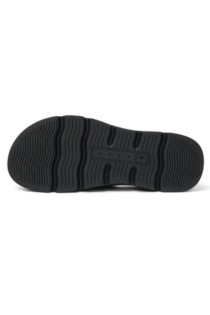 The image shows the black rubber outsole of the REEF Vista Luxe Vivianahh, featuring a wavy tread for grip and a central rectangular section with small raised letters—ideal for these vegan leather sandals with ergonomic design and cushioned footbed.