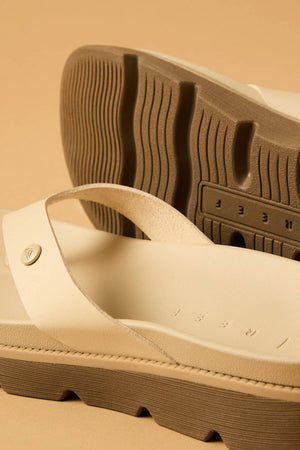 Close-up of two beige REEF Vista Luxe Vivianahh sandals with thick, textured brown soles and wide straps. One sandal lies flat and the other is propped up, showcasing the patterned sole, cushioned footbed, and indented branding on beige.