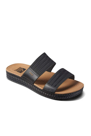 The REEF Water Vista Slide is a black sandal featuring two textured straps, a tan insole, and a woven-like design on the sole's edge. It has a flat base with dual density EVA footbed for added comfort, ideal for casual wear.