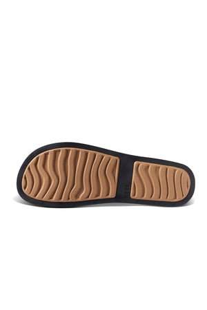 The REEF Water Vista Slide sandal features a black-bordered, textured tan sole. It's waterproof with wavy grooves for traction and a dual-density EVA footbed for comfort. "REEF" is embossed near the edge.
