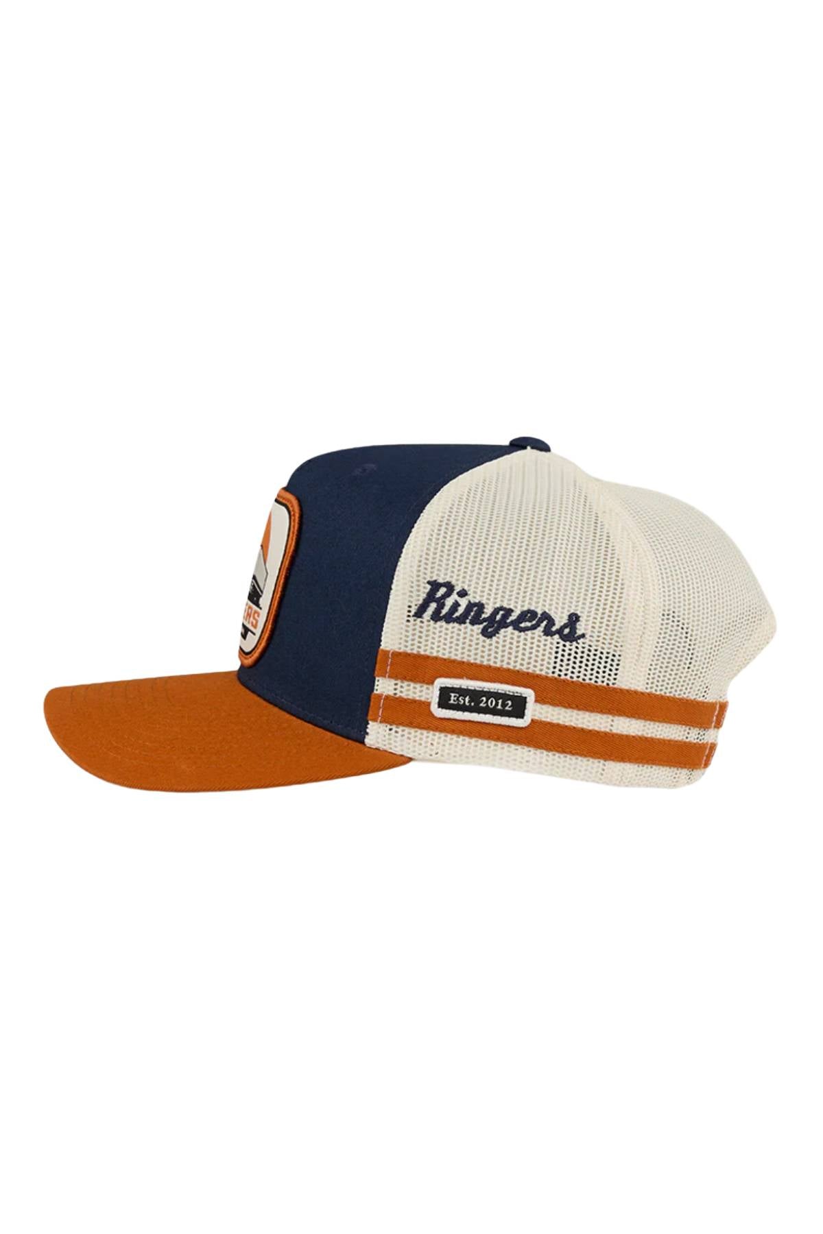 The Ringers Western Big Rig Trucker Cap features a navy front, brown brim, white mesh back, "Ringers" on the side, an "Est. 2012" patch with orange and white stripes, and an adjustable snapback for a custom fit.