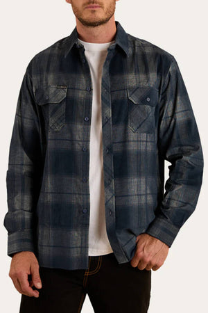 A man wears the Ringers Western Glenferrie Flannel Shirt in blue and gray plaid over a white t-shirt and black pants, one hand in his pocket. The 100% cotton shirt adds classic, laid-back style to his look.