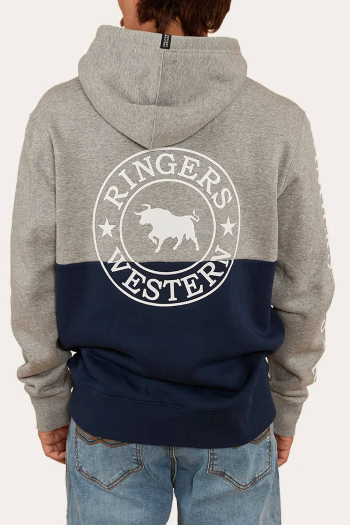 A person stands with their back to the camera wearing the Ringers Western Hahndorf Hoodie, a relaxed-fit, two-tone hoodie with a grey top, navy blue bottom, and a "Ringers Western" bull and stars logo.