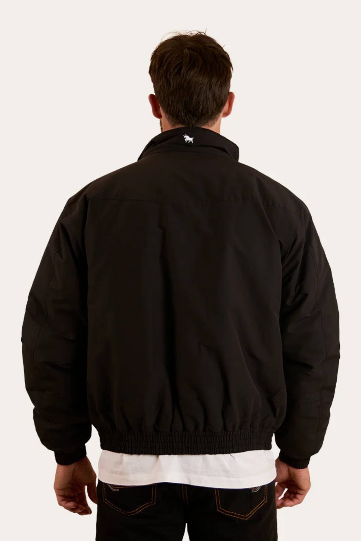 A man faces away from the camera wearing a black Ringers Western Kidman Jacket with a white shirt and dark jeans. The jacket features quilted lining and a small white animal logo on the upper back, set against a plain light background.