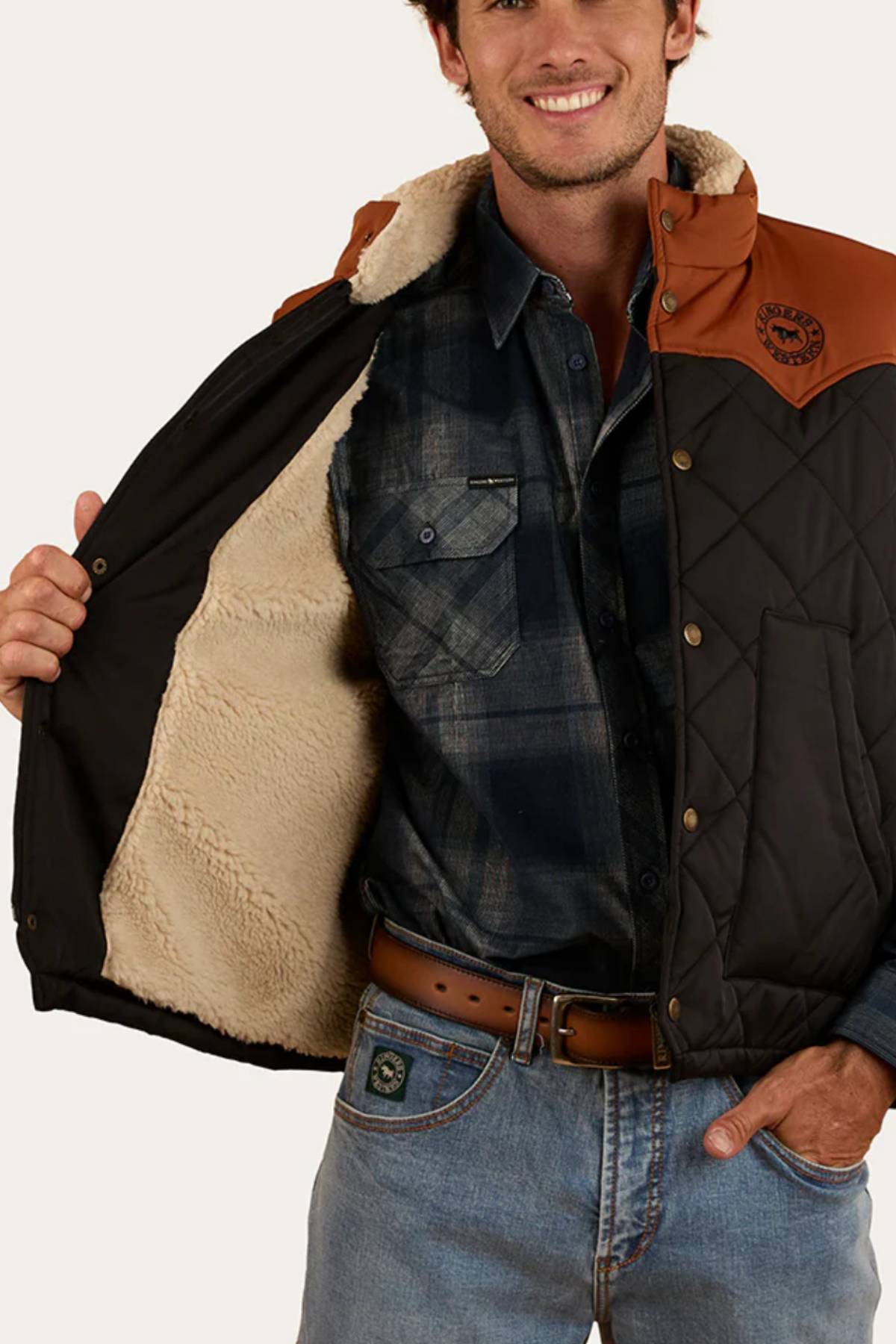 A man smiles while wearing the Ringers Western McKinlay Puffer Vest, holding it open to reveal its quilted design and faux shearling liningβideal for outdoor enthusiasts or fans of Ringers Western style.