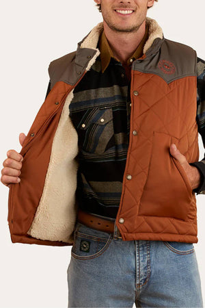 A man wearing jeans, a striped shirt, and the Ringers Western McKinlay Puffer Vest with a gray yoke opens it to reveal its fuzzy cream lining. This lightweight vest is perfect for outdoor enthusiasts. He smiles, his face partially visible.