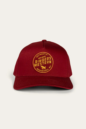 A front-facing image of the Ringers Western Rye Baseball Cap with a curved brim showcases its red design. The cap features a round, yellow embroidered patch on the front that reads "Authentic Ringers Western" and "Est. 2012, Wandoan, QLD," with a small bull icon centered within the patch. An adjustable strap at the back ensures a perfect fit.