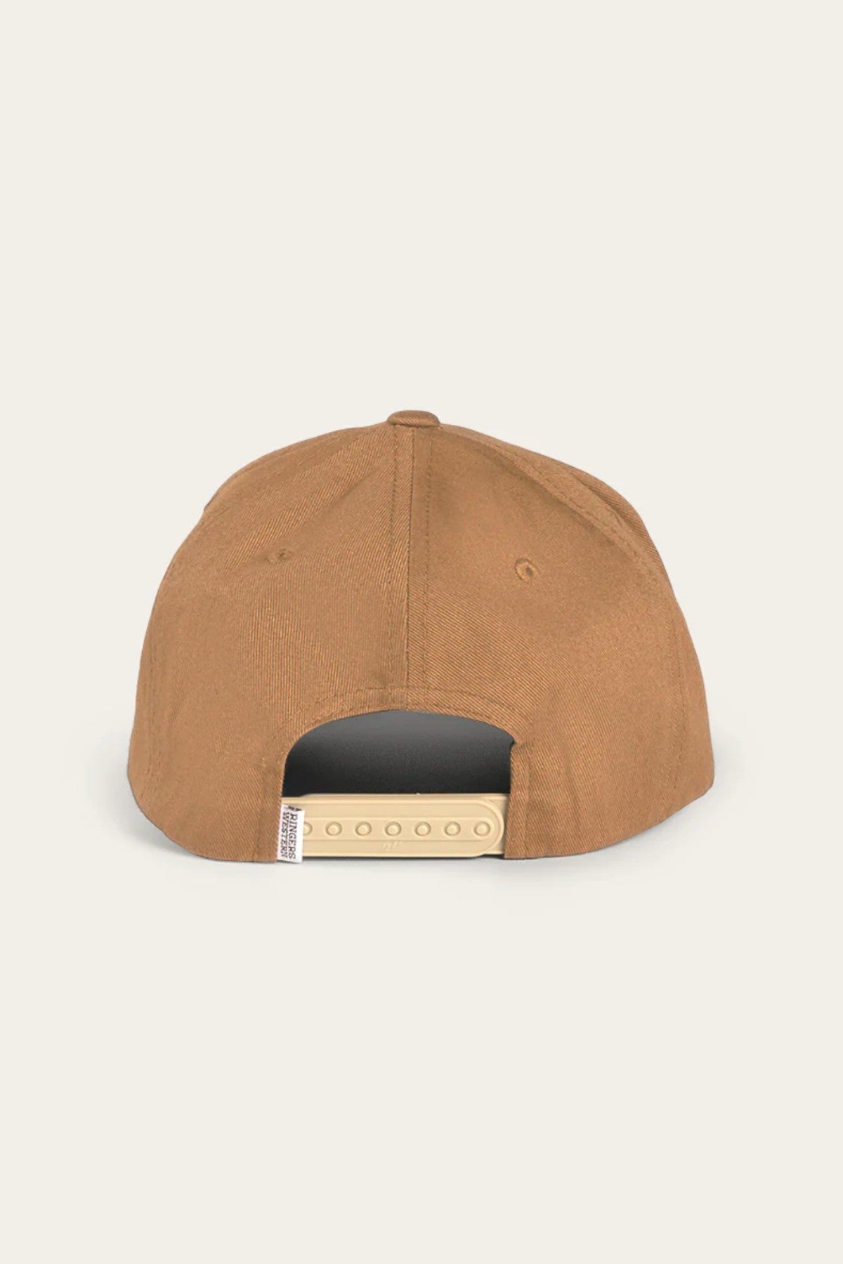 Rear view of the Ringers Western Rye Baseball Cap, made from brown cotton twill with a beige adjustable snapback closure. The cap showcases visible stitching and bears a small white Ringers Western label on the left side. The background is a plain, light-colored surface.