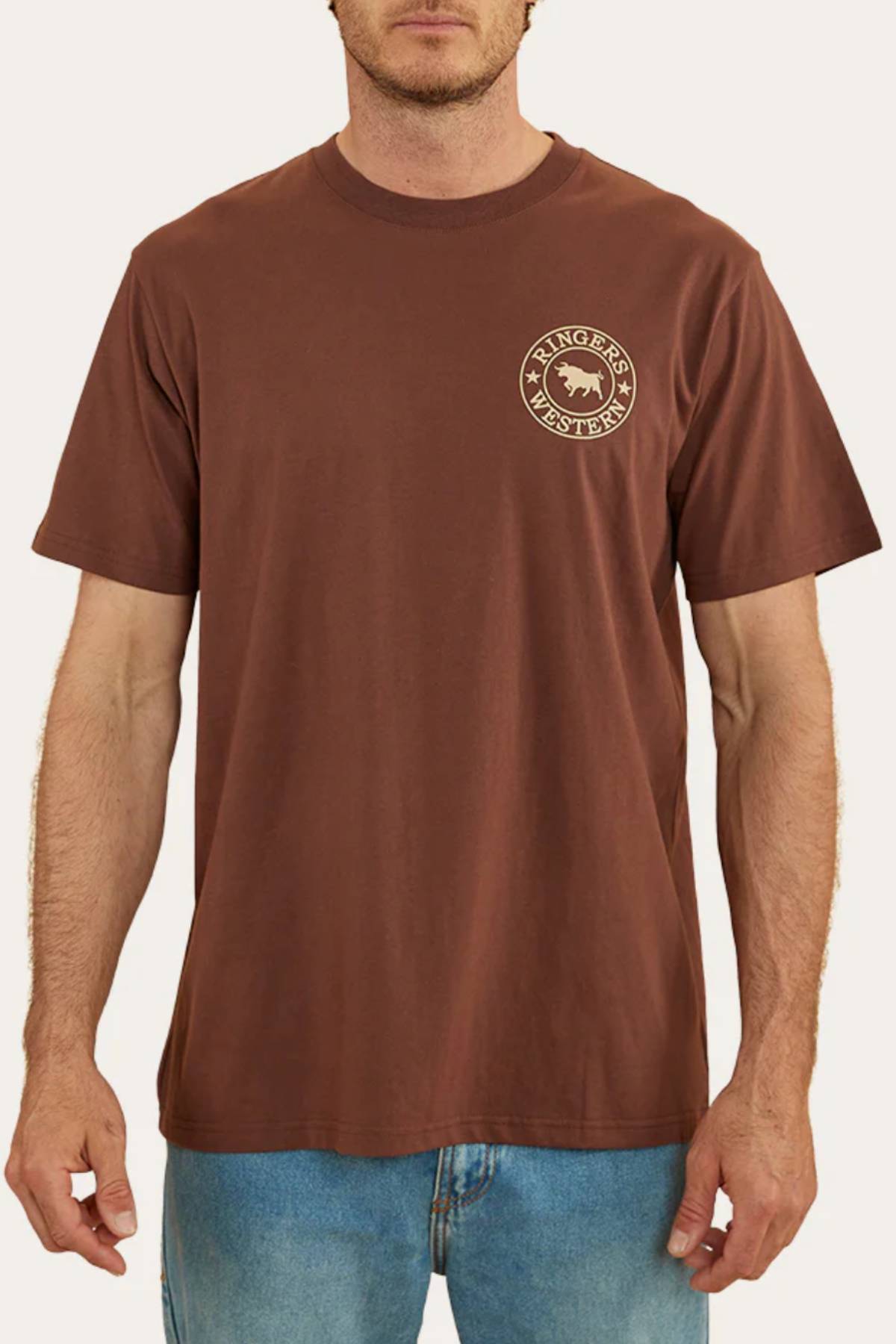 A man wears a brown Ringers Western Signature Bull Loose Fit T-Shirt, made from 100% cotton jersey with a small round bull logo on the left chest, paired with blue jeans against a plain background.