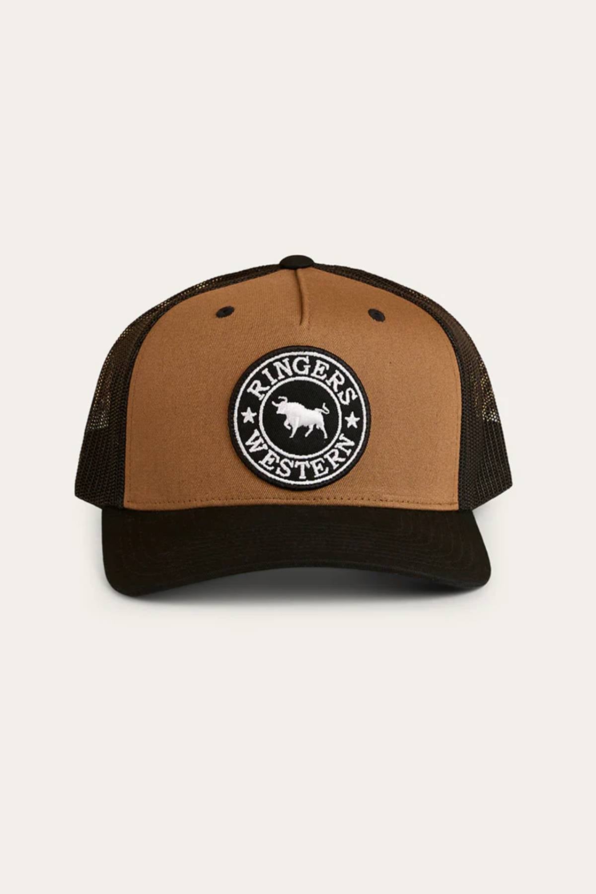 The Ringers Western Signature Bull Trucker Cap is brown and black with a circular white bull patch on the front. It features a mesh back, curved brim, and adjustable strap for a comfortable fit.