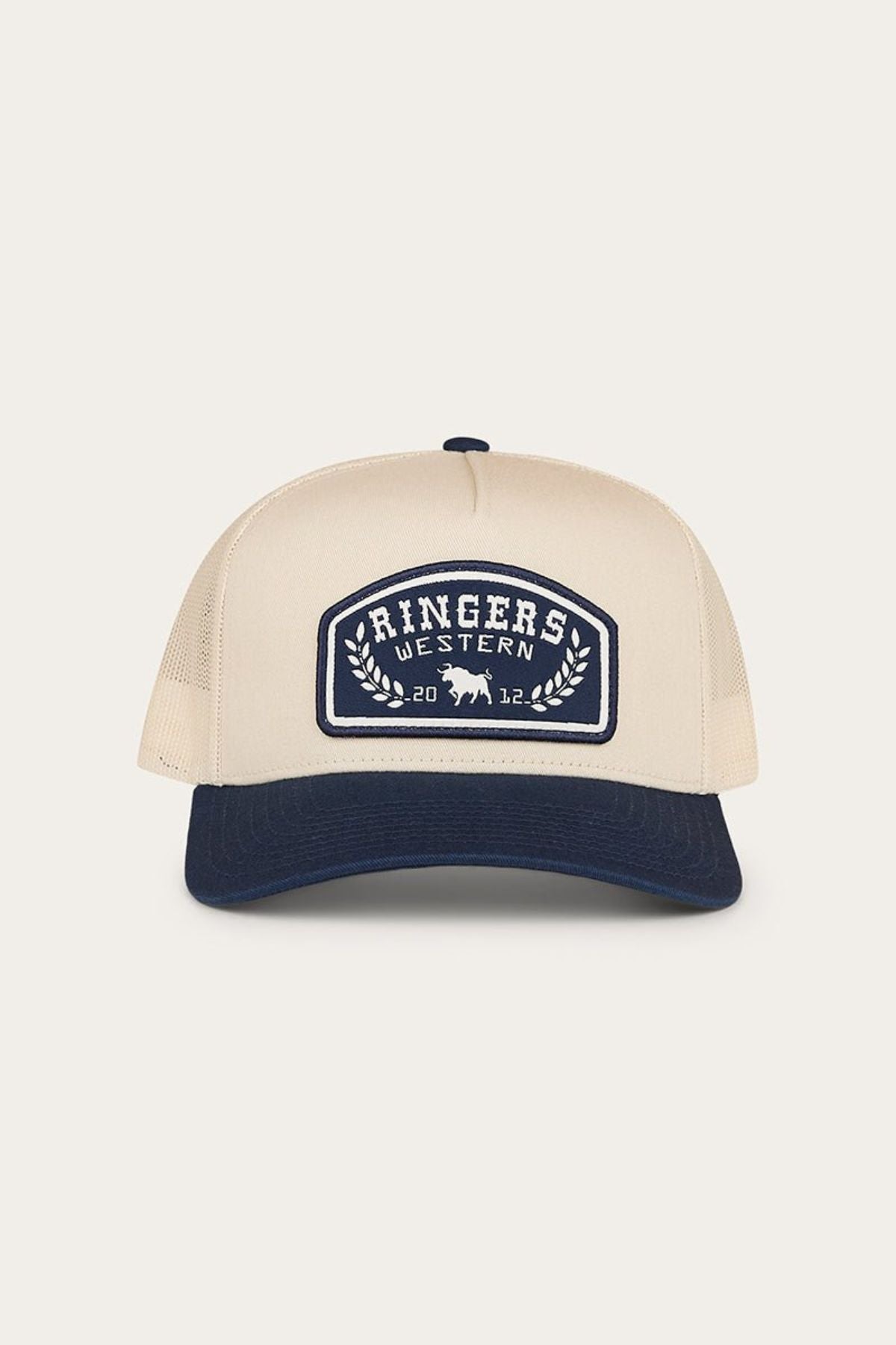 The Ringers Western Wheatbelt Trucker Cap is displayed from the front against a plain background, featuring a beige and navy color scheme, a patch with “Ringers Western 2022” and a bull logo. This cap offers a mid-profile silhouette and an adjustable snapback closure for comfort.