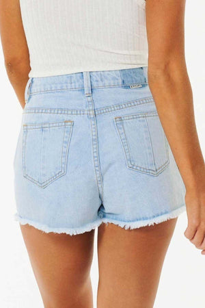A person is shown from the back wearing the "Rip Curl Amy High Waist Short" in light blue denim, featuring a high waist and frayed hems, paired with a sleeveless white top against a plain white background that subtly evokes summer adventures.
