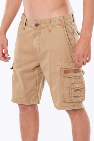 A person stands against a plain white background wearing Rip Curl Classic Surf Trail Cargo Shorts in a relaxed fit. The cotton shorts are designed with multiple pockets, a button and zipper closure, and have a logo patch on one pocket.