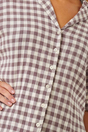Close-up of an ocean enthusiast wearing a button-up Rip Curl Premium Surf Check Shirt featuring a checkered pattern in brown and white. One hand is placed on their hip, highlighting the collar and buttons along the front. The textured fabric is made from 100% cotton.