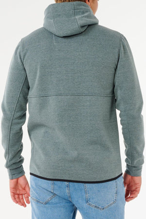 A person wears a Rip Curl Anti Series Departed Zip Thru, a water-resistant winter hoodie, paired with light blue jeans and shown from the back against a plain white background.