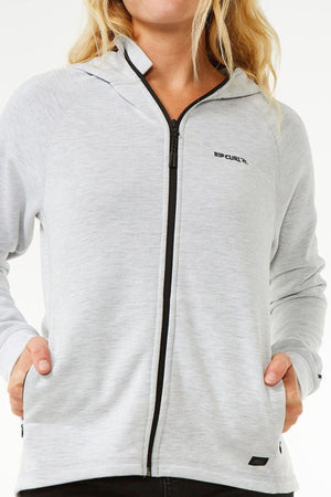 A person wearing a light gray Rip Curl Anti Series Flux III Jacket zip-up hoodie with a hood, black zipper, and hands in side pockets, shown from shoulders to hips against a white background.