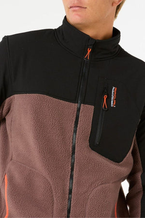 A person wears the Rip Curl Anti Series Search Zip Crew, featuring a black upper, brown polyester polar fleece lower section, zippered chest pocket with orange accents, and visible logo. The person's face is partially out of frame.