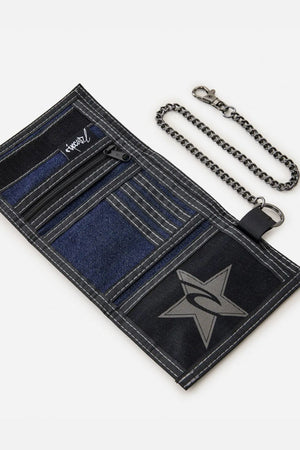 The Rip Curl Archive Denim Surf Wallet, shown open and flat on a white background, features black and blue cotton denim, multiple compartments, white stitching, a star and swoosh design, and an attached metal chain with clasp.