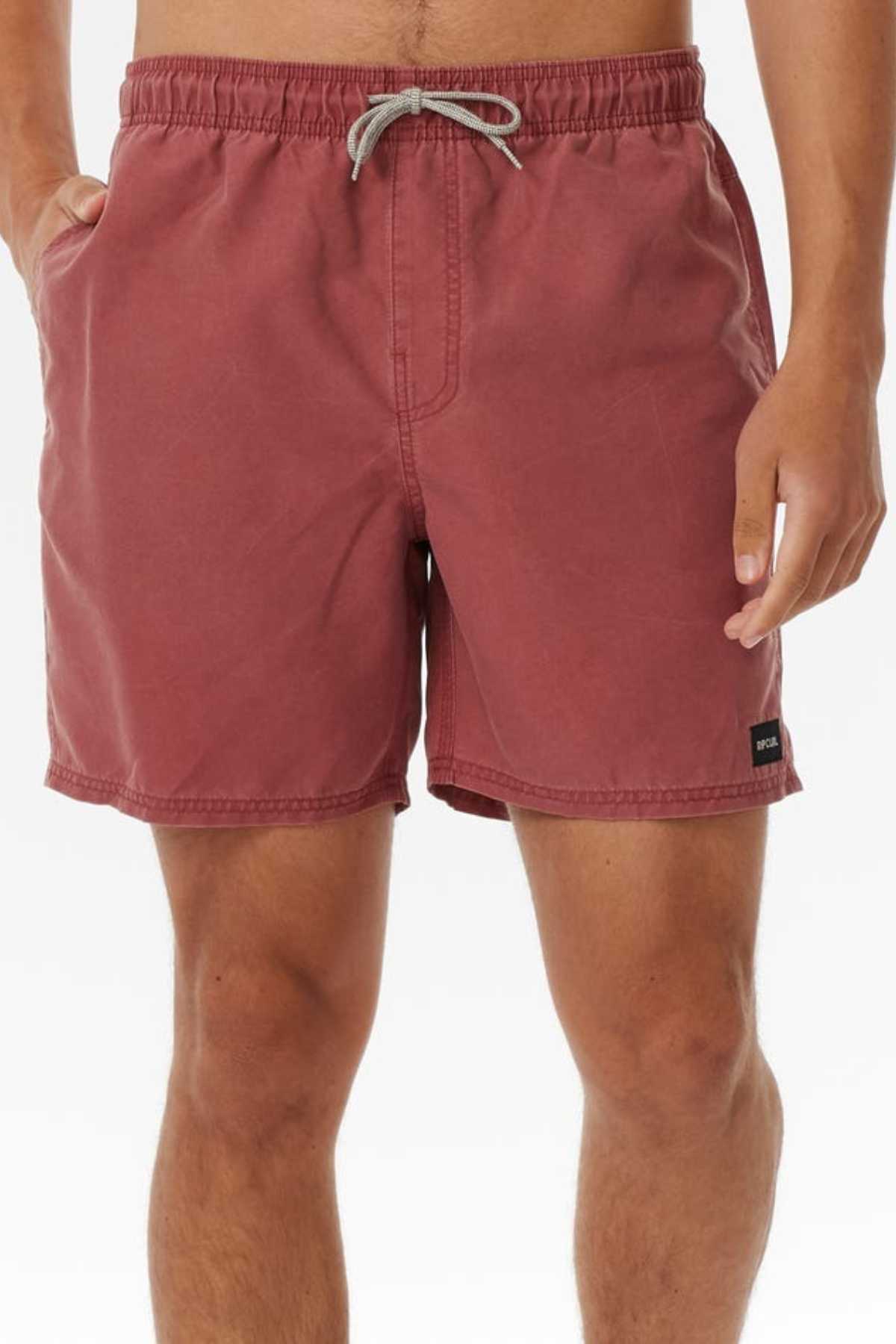 A person wearing knee-length Rip Curl Bondi Volley shorts, in dusty rose made from recycled PET, featuring an elastic waistband with drawstring, side pockets, and a small black patch label on the lower left side against a plain white background.
