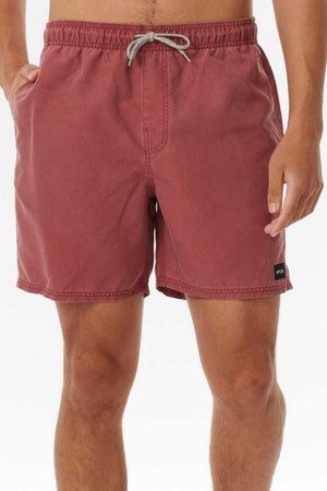 A person wearing knee-length Rip Curl Bondi Volley shorts, in dusty rose made from recycled PET, featuring an elastic waistband with drawstring, side pockets, and a small black patch label on the lower left side against a plain white background.