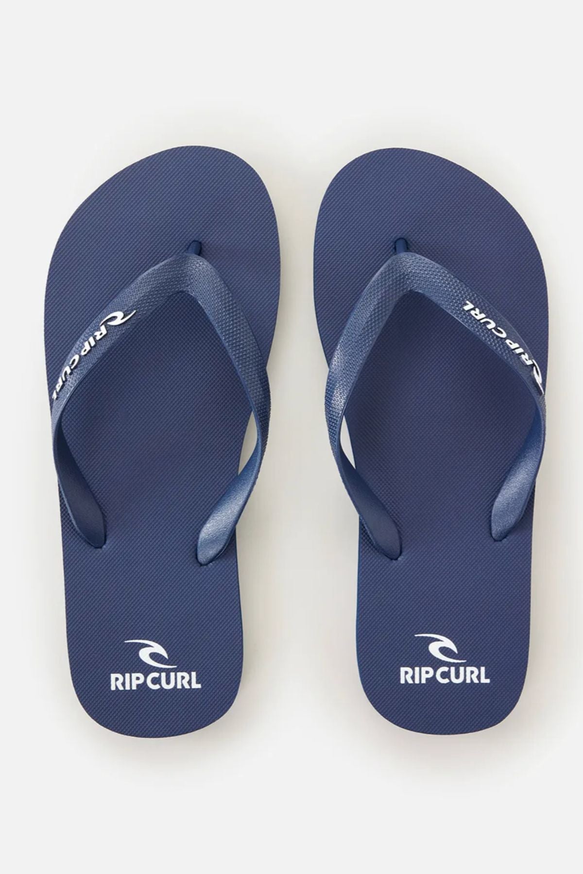 A pair of Rip Curl Brand Logo Bloom Thongs in blue, made with eco-friendly algae-blended foam and white brand logos on the heel and strap, displayed side by side on a plain white background.