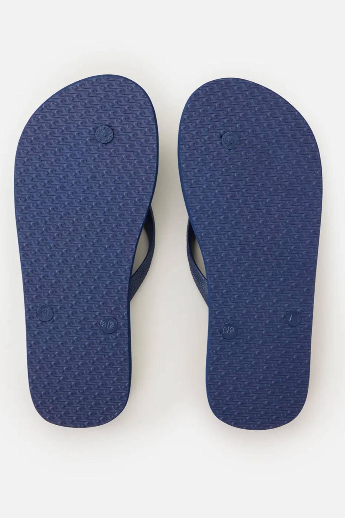 A pair of navy blue Rip Curl Brand Logo Bloom Thongs made with algae-blended foam and small circular textured soles are shown from the bottom, side by side on a plain white background.