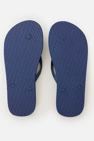 A pair of navy blue Rip Curl Brand Logo Bloom Thongs made with algae-blended foam and small circular textured soles are shown from the bottom, side by side on a plain white background.
