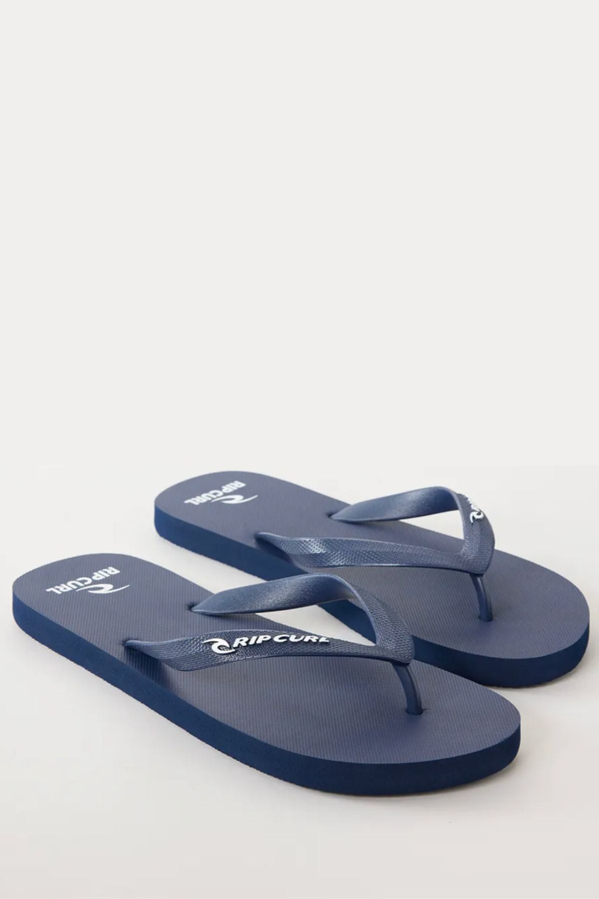 A pair of Rip Curl Brand Logo Bloom Thongs in blue, featuring white "Rip Curl" logos on the straps and footbeds, made from eco-friendly algae-blended foam, displayed on a plain white surface.