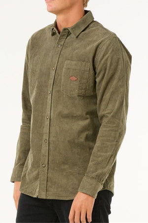 A person wears an olive green Rip Curl Classic Surf Cord Shirt with a chest pocket and black pants, standing against a plain light background.