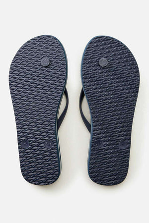 A pair of Rip Curl Classic Surf Bloom Thongs in dark blue, featuring BLOOM algae-blended foam and ergonomic molded straps, is shown from the bottom and displayed side by side on a light gray background.