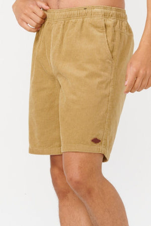 A person wears Rip Curl Classic Surf Cord Volley shorts—OG fit tan cotton corduroy with an elastic waistband, side pockets, and a small brown patch above the left hem. Ideal for beach casual wear. The background is plain white.