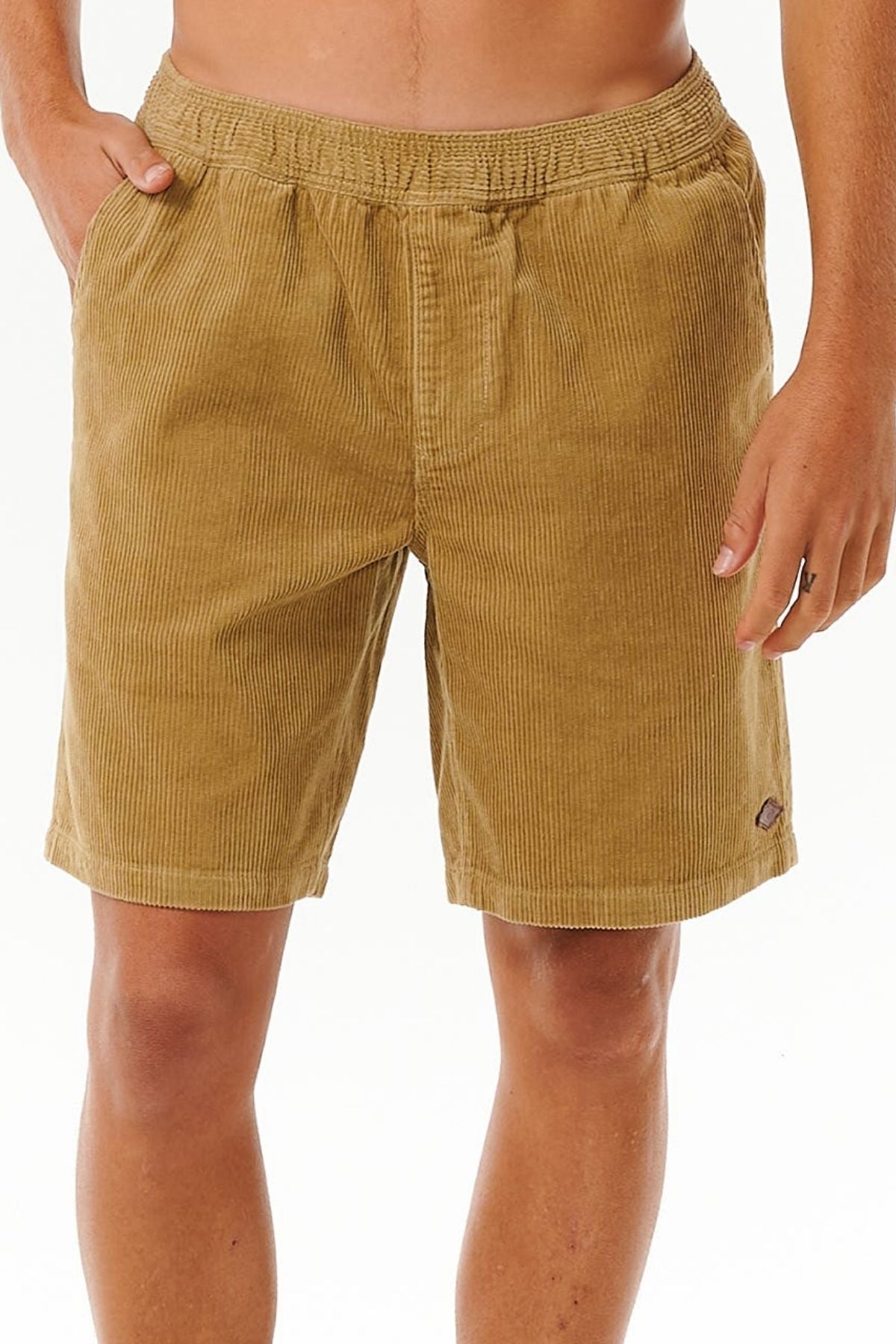 Wearing Rip Curl Classic Surf Cord Volley shorts with an elastic waistband, a person stands hands-in-pockets against a plain white background, showing only the lower torso and upper legs of these vintage-style corduroy shorts.