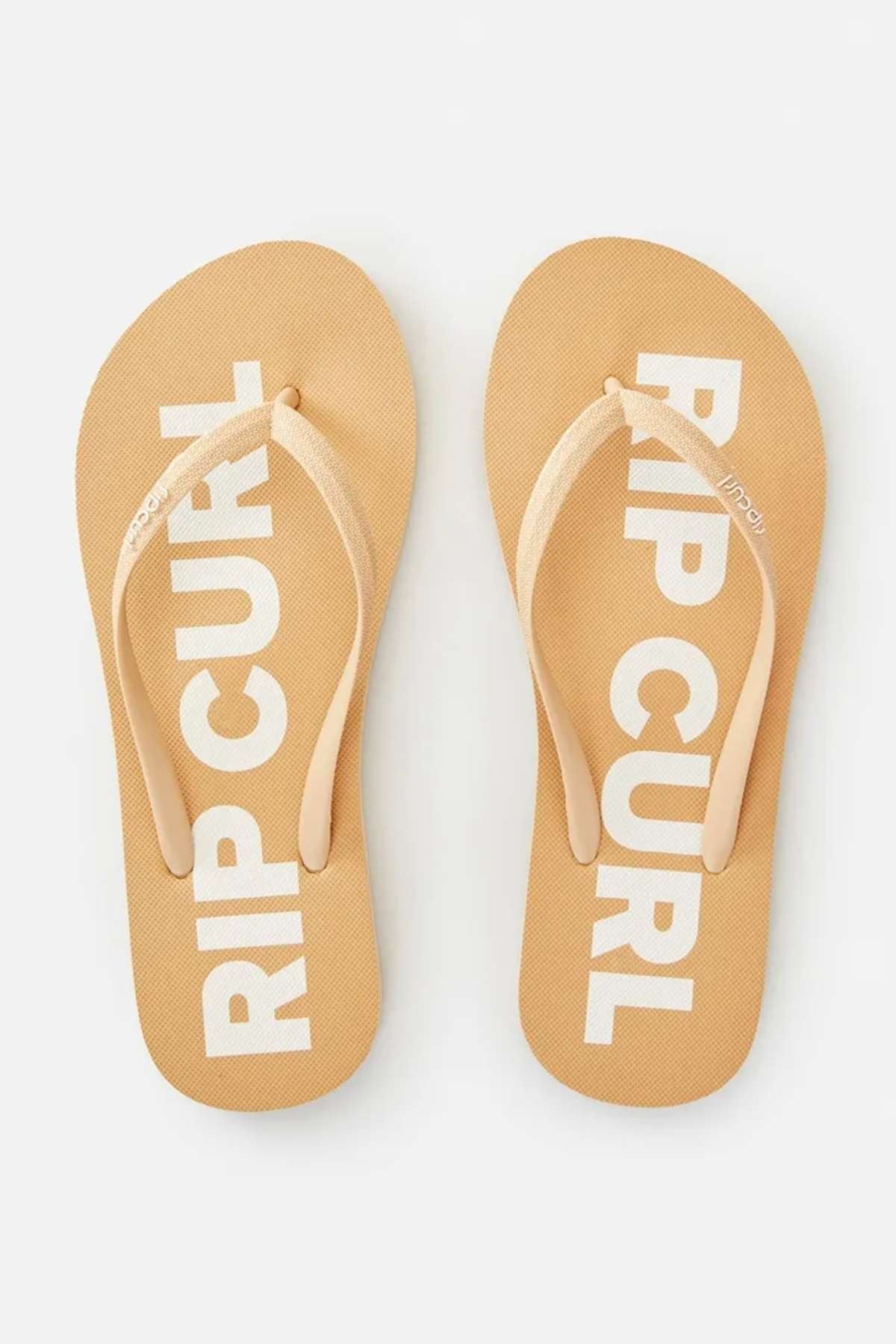 A pair of beige Rip Curl Classic Surf Thongs, featuring "RIP CURL" prominently displayed on the ergonomic molded straps and soles, are positioned side by side on a light background.