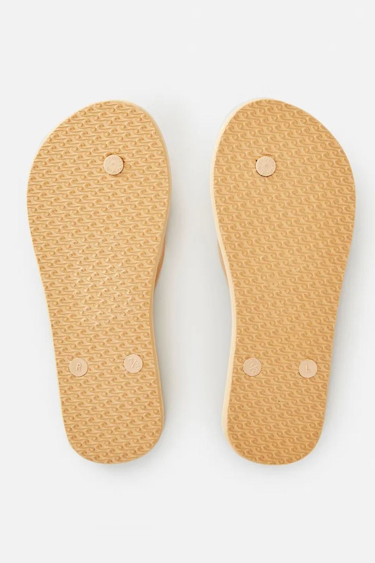 The image showcases the textured soles of two beige Rip Curl Classic Surf Thongs, clearly labeled with "R" for right and "L" for left. The ergonomic molded strap harmonizes with the repeating pattern on each sole, with the flip-flops aligned side by side.