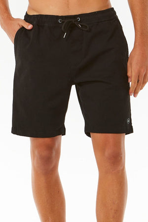 A person showcases the Rip Curl Classic Surf Volley black swim trunks, featuring a flexible fit and pockets, standing against a plain white background. Only the lower torso and legs are shown.
