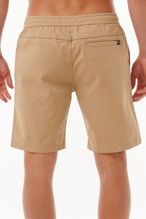 A person is wearing Rip Curl Classic Surf Volley shorts, light brown cotton with an elastic waistband and adjustable drawcord for a flexible fit, featuring a back zipper pocket on the right. The background is plain white.