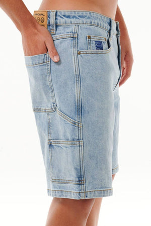 A person wearing light blue Rip Curl Dosed Denim Walkshorts with multiple pockets, including a side pocket and a small label above the right front pocket, stands against a plain white background.