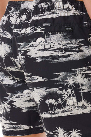 Close-up of the Rip Curl Dreamers Volley board shorts in black and white, showcasing an all-over print of a tropical beach scene with palm trees, clouds, and a setting sun. Crafted from recycled fabric, the back pocket features a tag that reads "Rip Curl.
