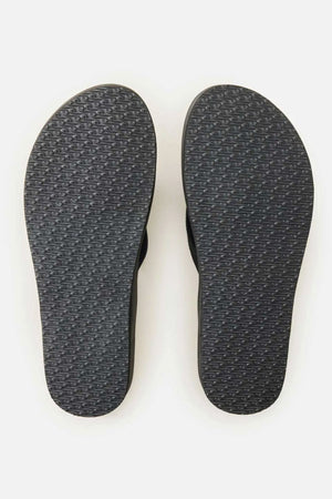 A pair of black Rip Curl Essential Contour Bloom Thongs shown side by side, soles up, displaying their textured rubber with an oval pattern and contoured footbed, set against a plain light background.