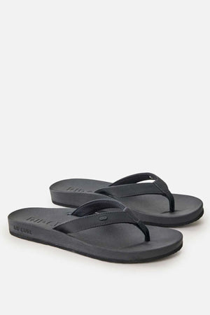 A pair of Rip Curl Essential Contour Bloom Thongs in black with thin straps and a flat sole, displayed on a plain white background. The Rip Curl brand name is embossed on the side for a sleek finish.