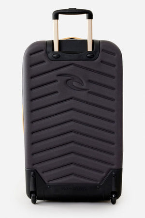 A black Rip Curl F-Light Global 100L Tropics Travel Bag with a chevron pattern, hard shell, lockable zips, two wheels, telescopic handle, and subtle embossed logo stands upright against a plain white background.