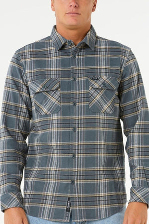 A person wearing the Rip Curl Griffin Flannel Shirt—a long-sleeved blue and gray cotton flannel with buttoned chest pockets—stands against a plain white background.