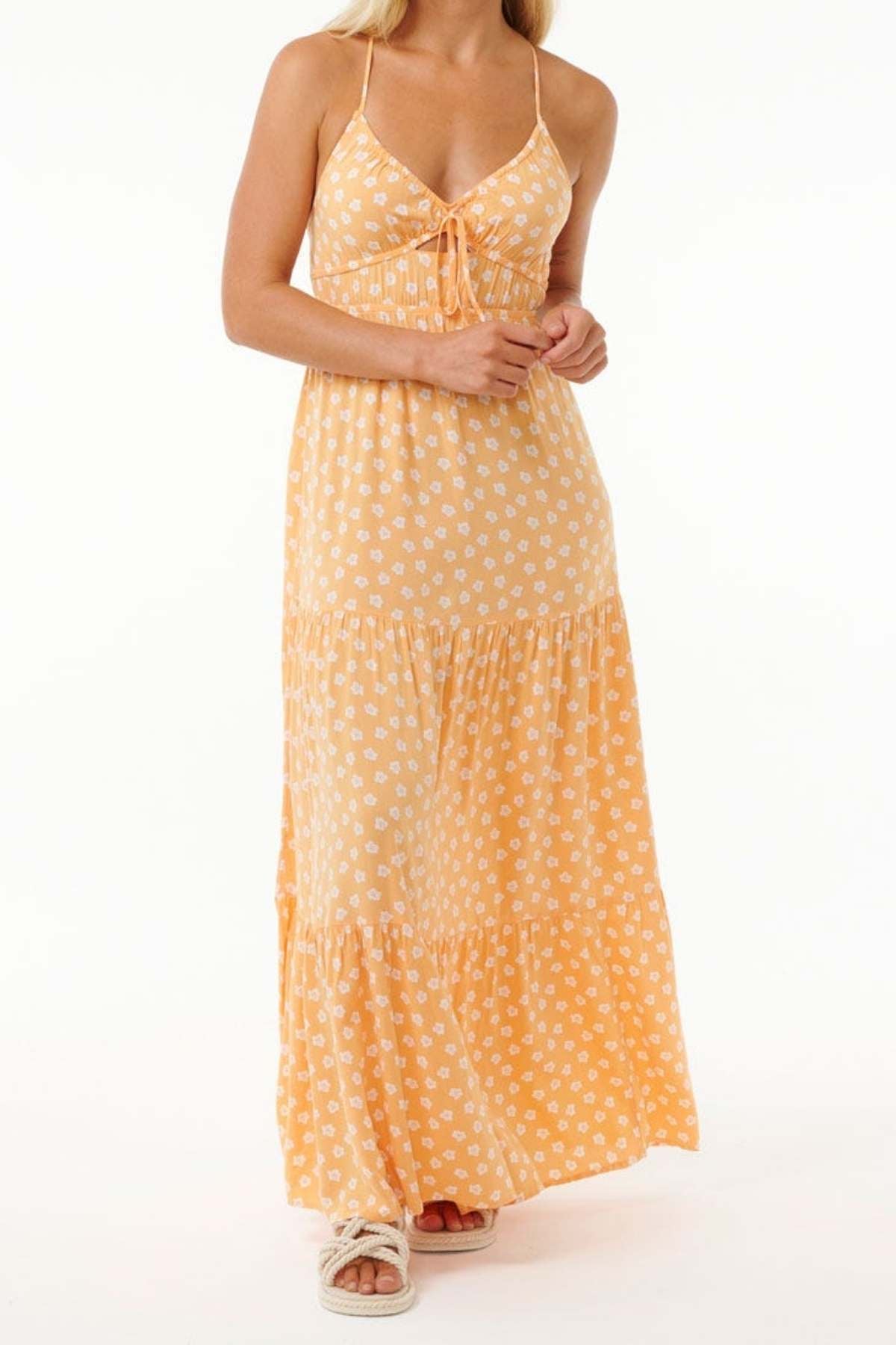 A person wearing a long, sleeveless, orange dress adorned with white floral patterns exudes a breezy style reminiscent of the Rip Curl High Tide Ditsy Maxi Skirt. The dress highlights a tied front and tiered design, complemented by white sandals on a plain white background.