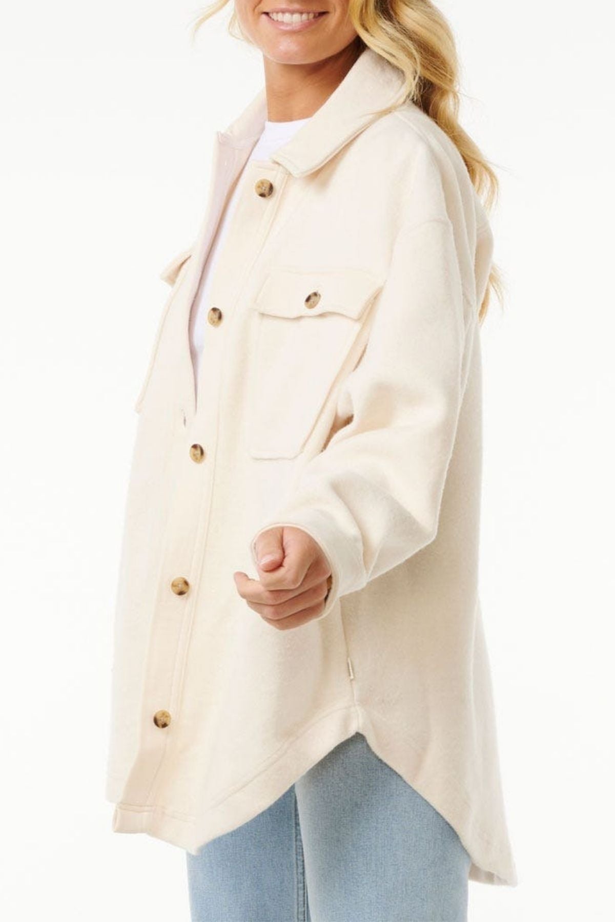 A woman smiles in a cream Rip Curl High Tide Fleece Shacket with flap pockets and light blue jeans, standing against a white background—ideal for adventurous spirits.